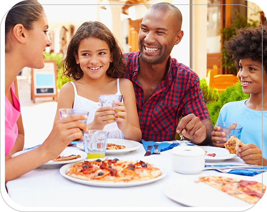 A family sitting at an outdoor table eating pizza.